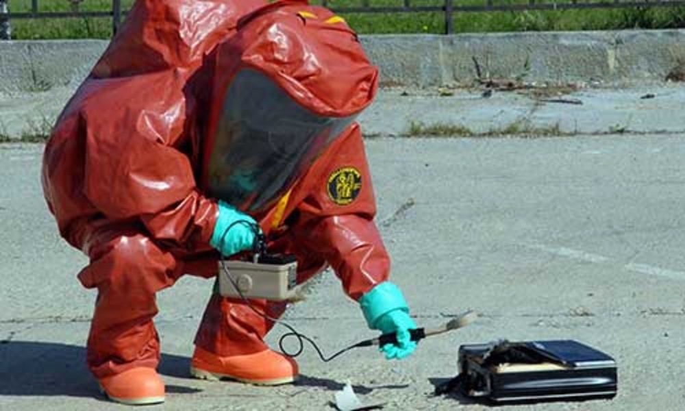 A specialist in a red protective suit conducts readings with detection equipment during a chemical, biological, radiological, or nuclear response exercise. A specialist in a red protective suit conducts readings with detection equipment during a chemical, biological, radiological, or nuclear response exercise.