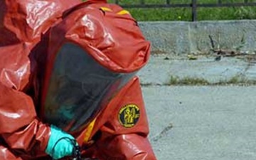 A specialist in a red protective suit conducts readings with detection equipment during a chemical, biological, radiological, or nuclear response exercise.