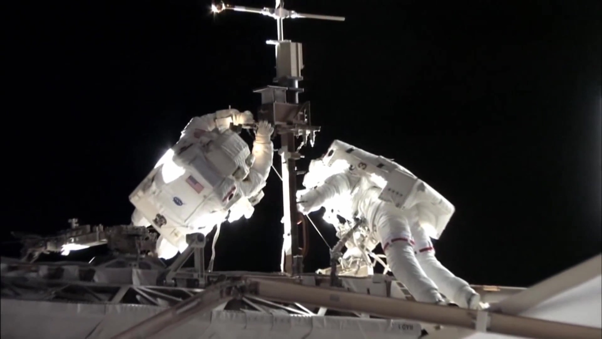 Two astronauts work on equipment while on the moon.