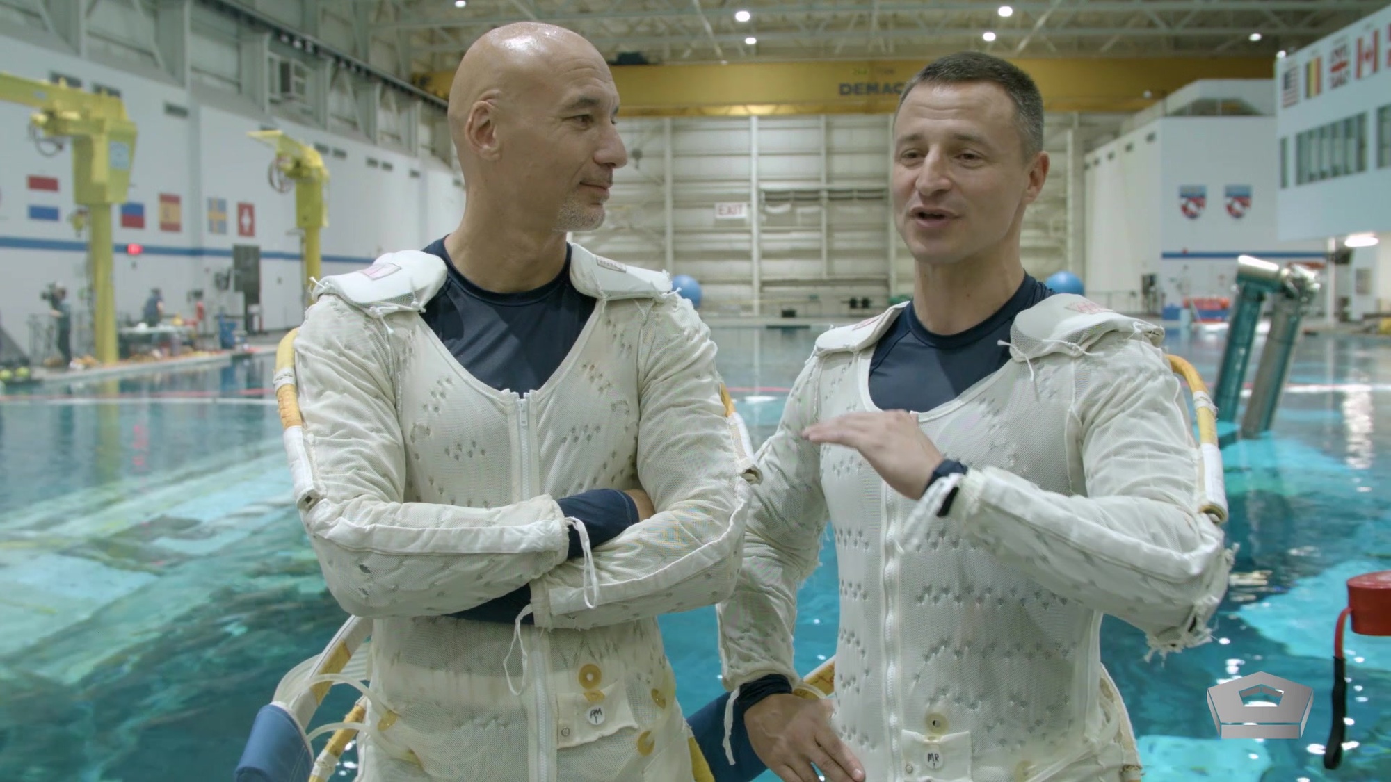 Two astronauts are stand in front of a pool.