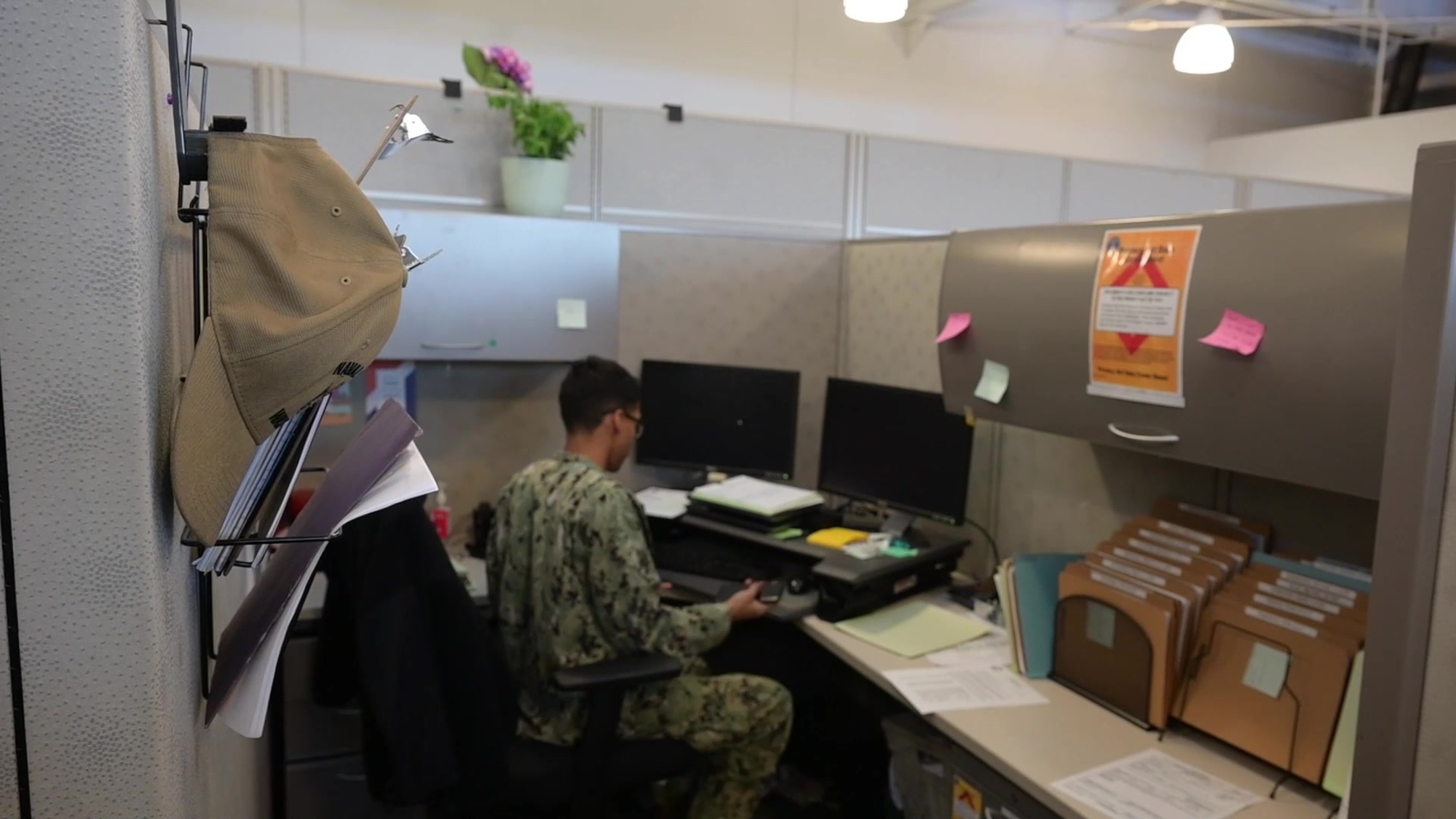 A sailor sits at a desk in a cubicle.