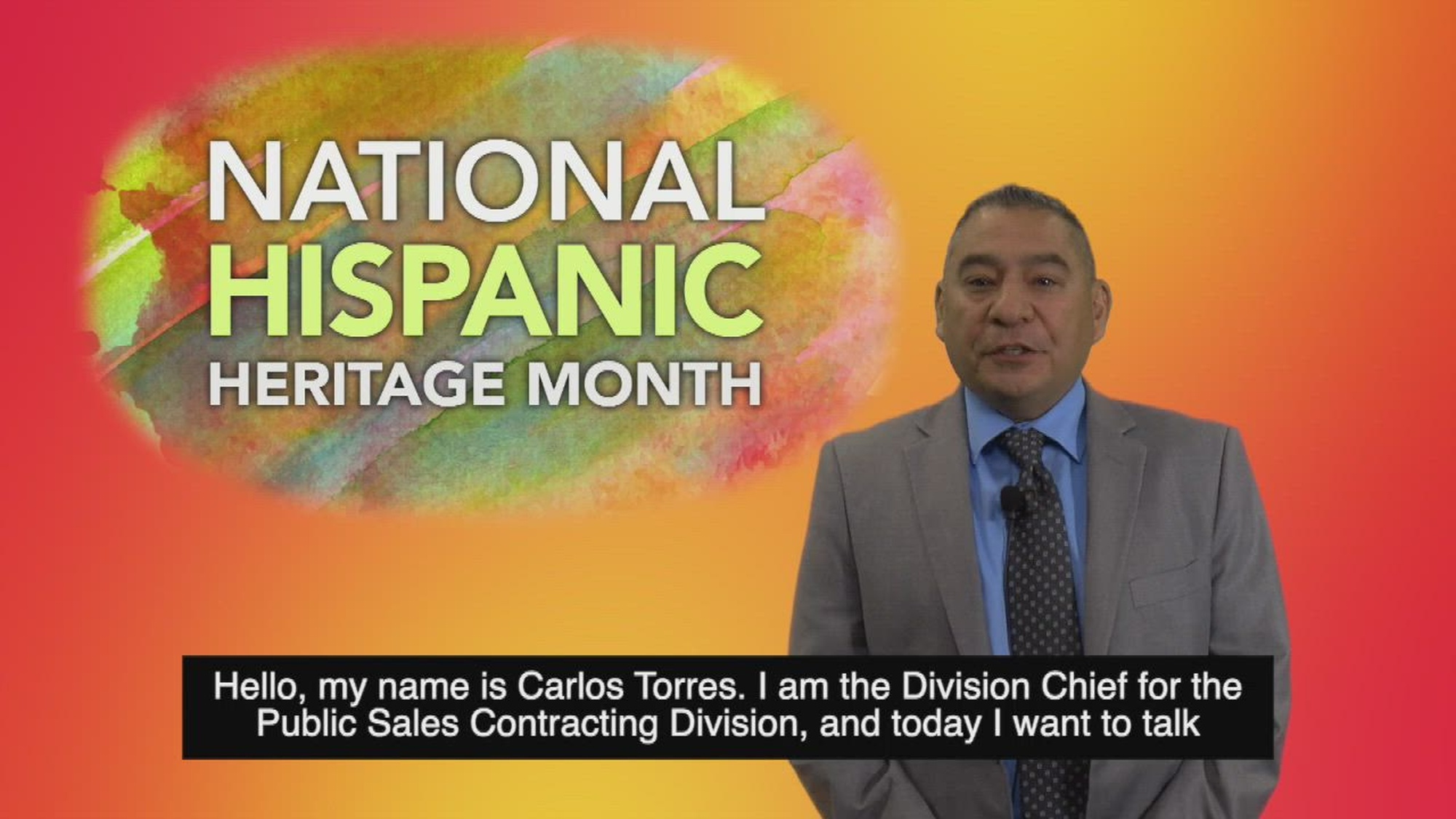 A civilian speaks in front of an orange background with the words "NATIONAL HISPANIC HERITAGE MONTH."
