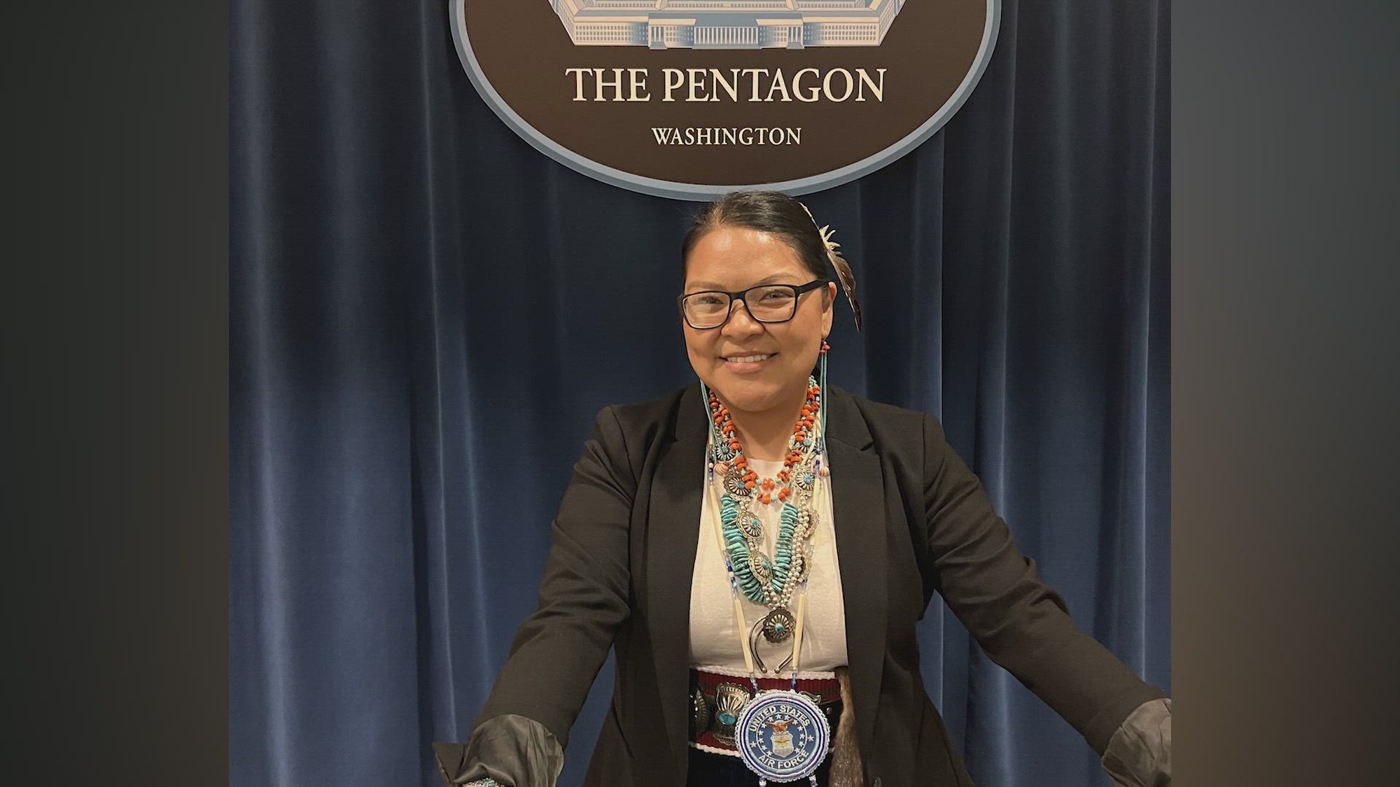 A person in Native American garb smiles under a Pentagon seal. 