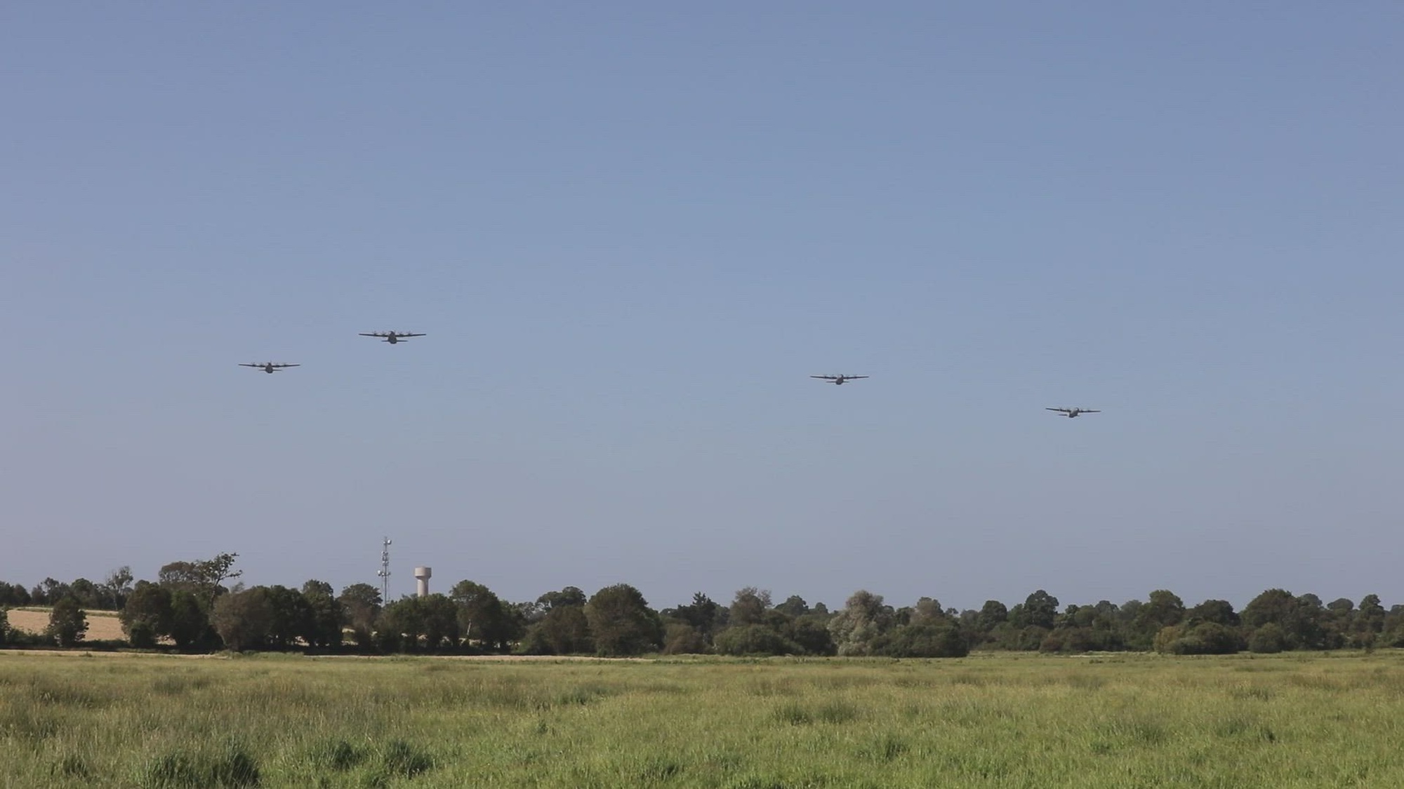 Aircraft fly in formation across a field. 