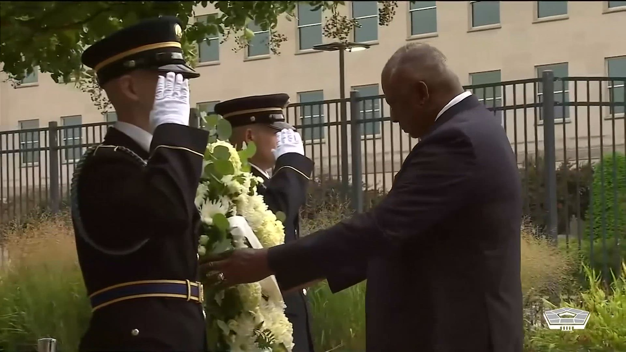 Secretary of Defense Lloyd J. Austin III places a wreath outside the Pentagon as two service members salute.