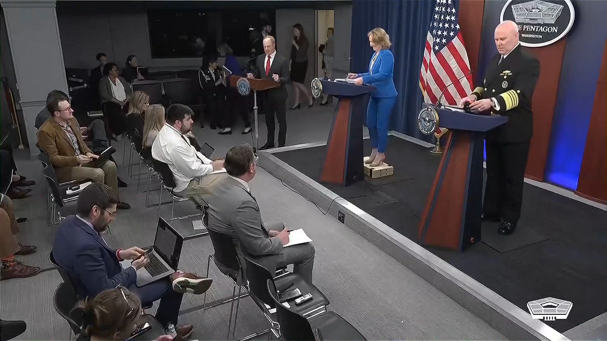 Deputy Secretary of Defense Kathleen Hicks and Joint Chiefs of Staff Vice Chairman Navy Adm. Christopher W. Grady stand at podiums at the Pentagon with reporters in chairs facing them.