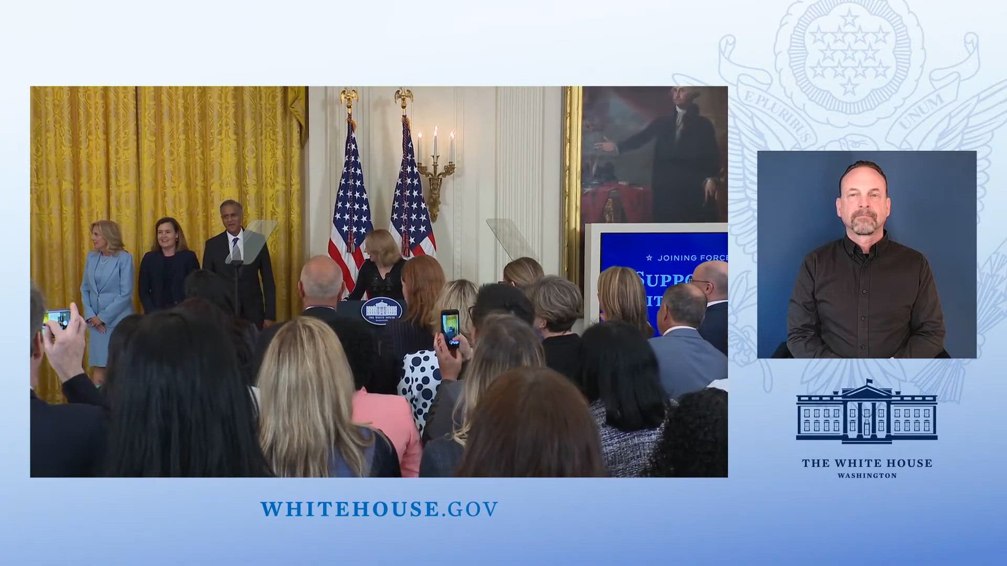 Image of people standing on stage in front of an audience embedded in a White House graphic frame.
