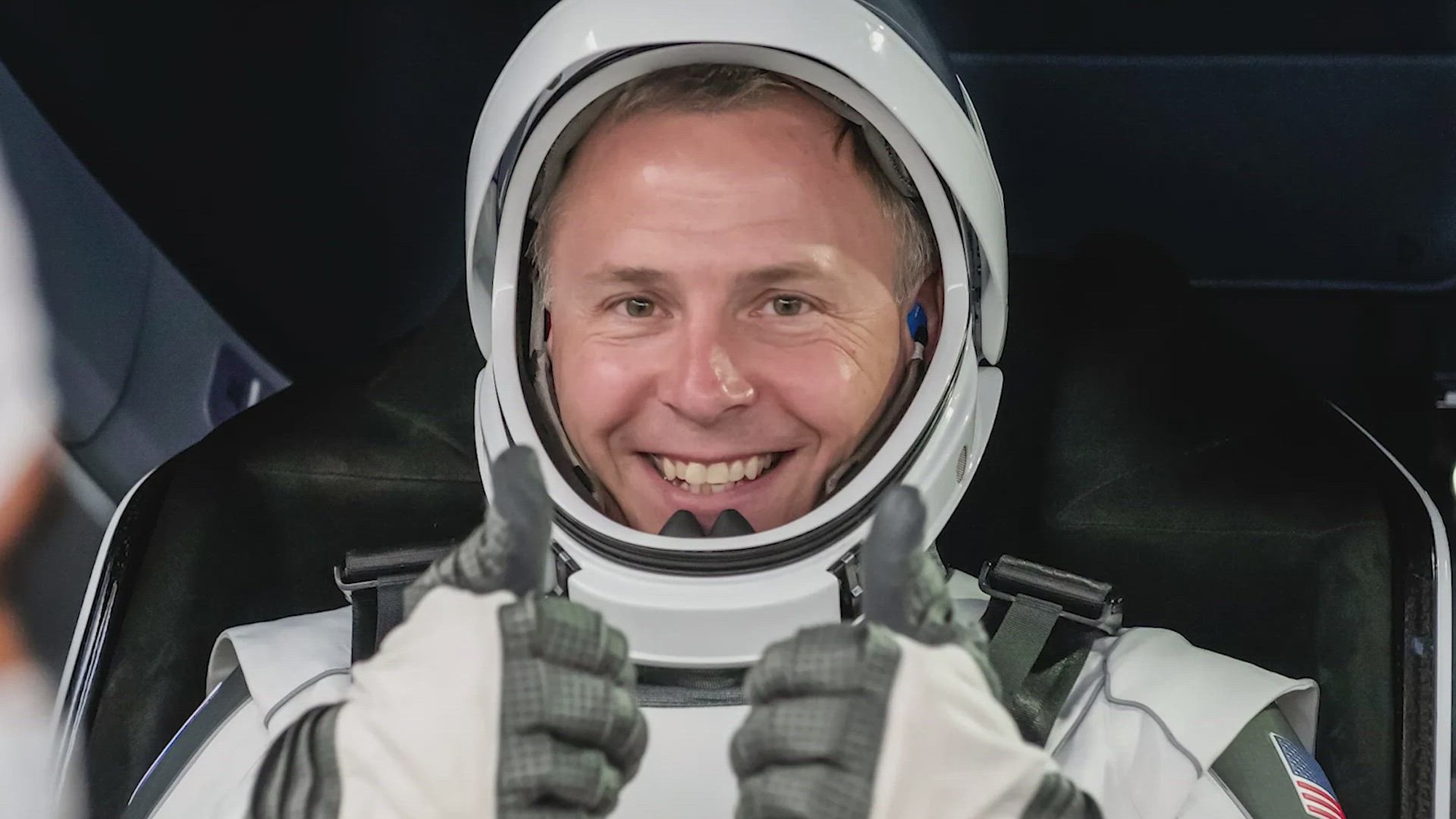 A male astronaut is smiling and giving two thumbs up.