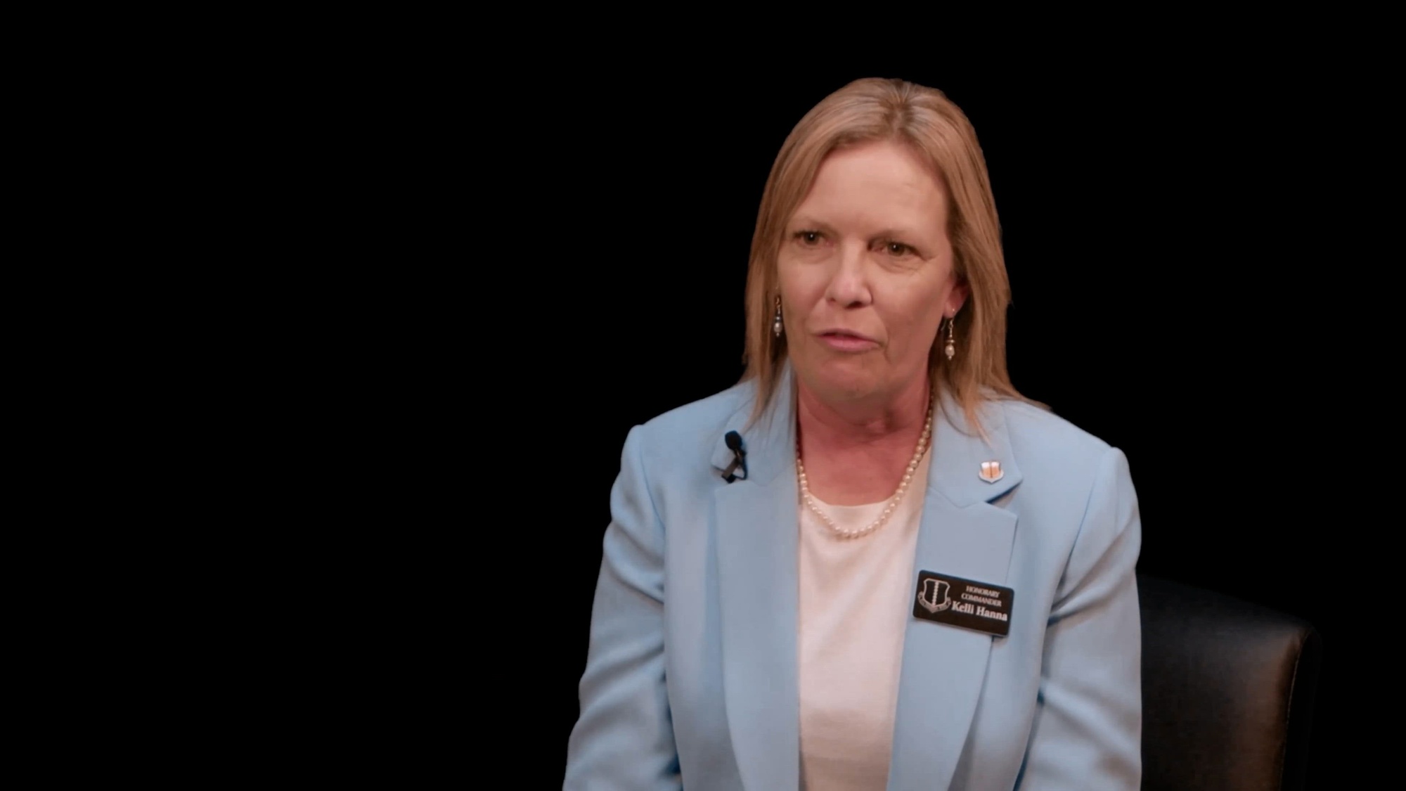 A woman with a light blue blazer is sitting for an on-camera video interview.  