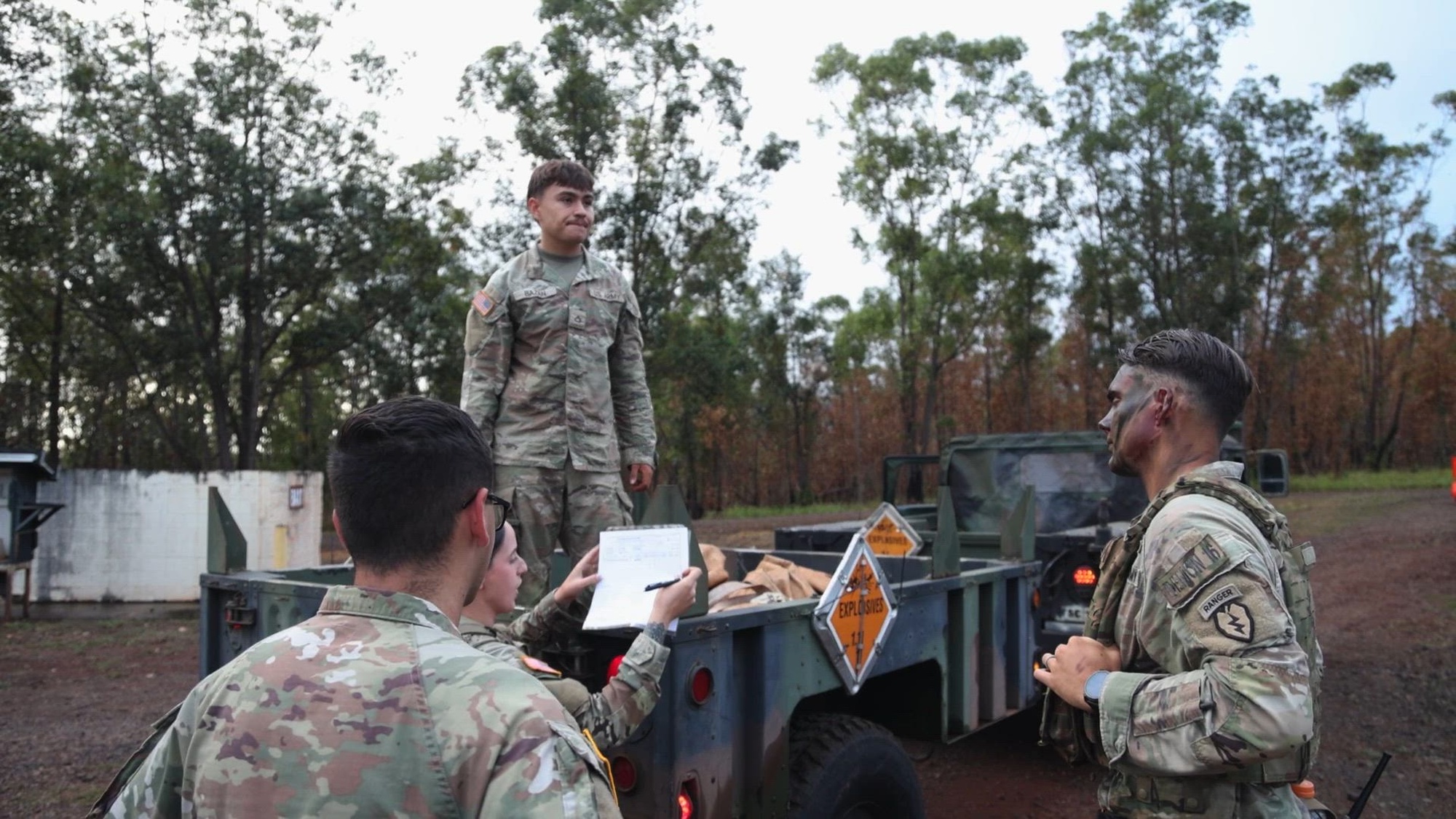 A group of soldiers stands in front of a military vehicle