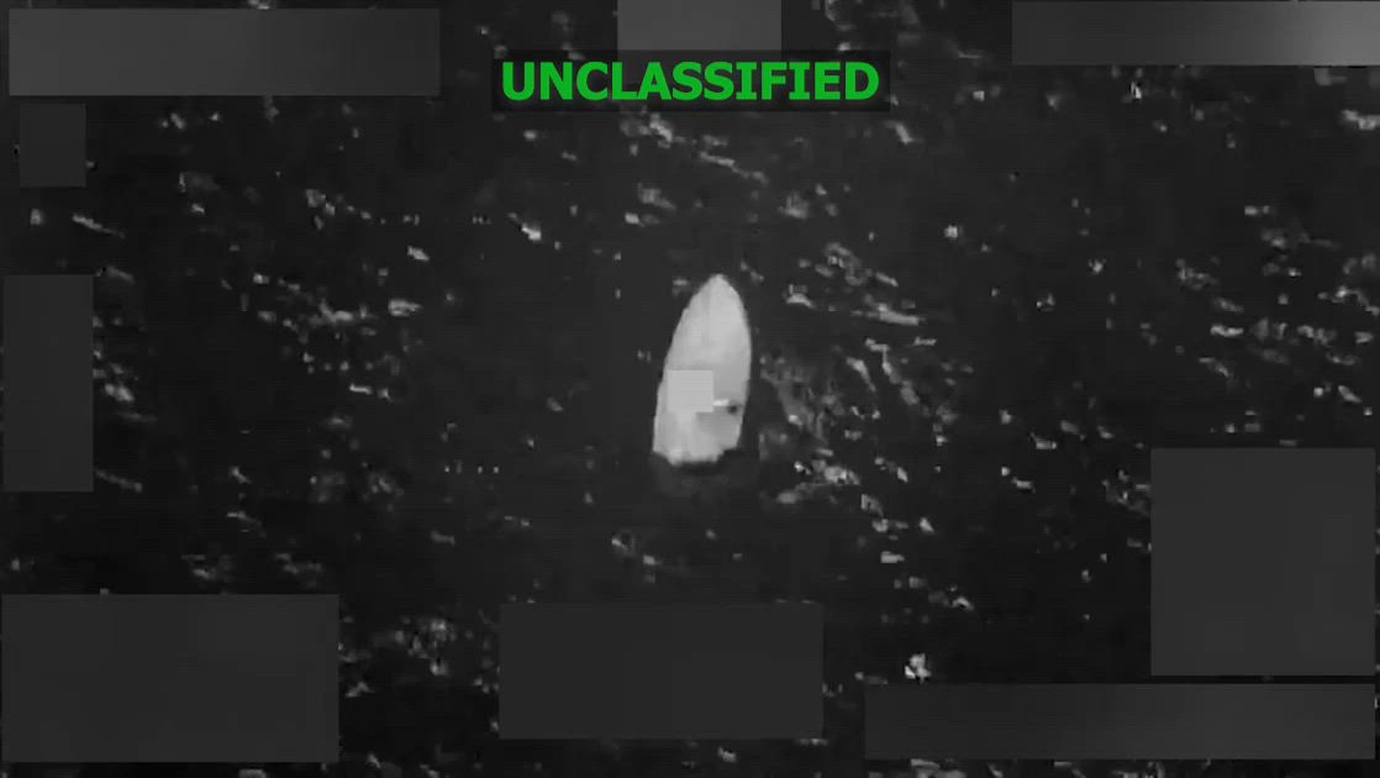 Black and white overhead footage of a boat being struck by munitions.