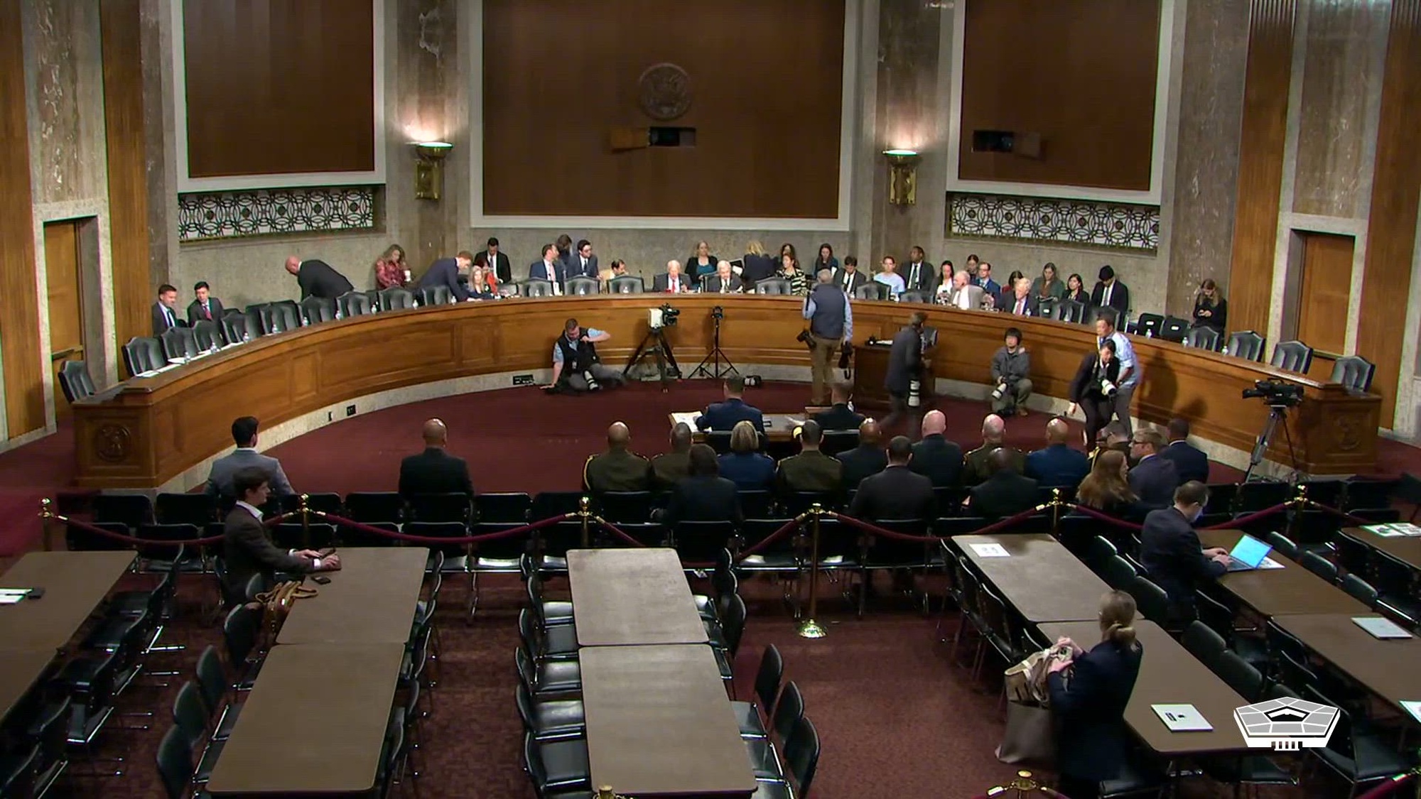 People sit at a curved table in a large room facing other tables and chairs. 