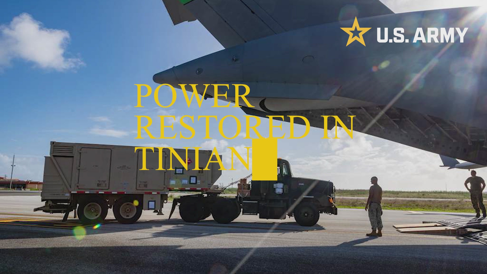 A truck carrying equipment is parked near the tail of an Army aircraft on a runway, with two soldiers looking at it.