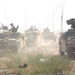 Vehicles follow Soldiers through a field