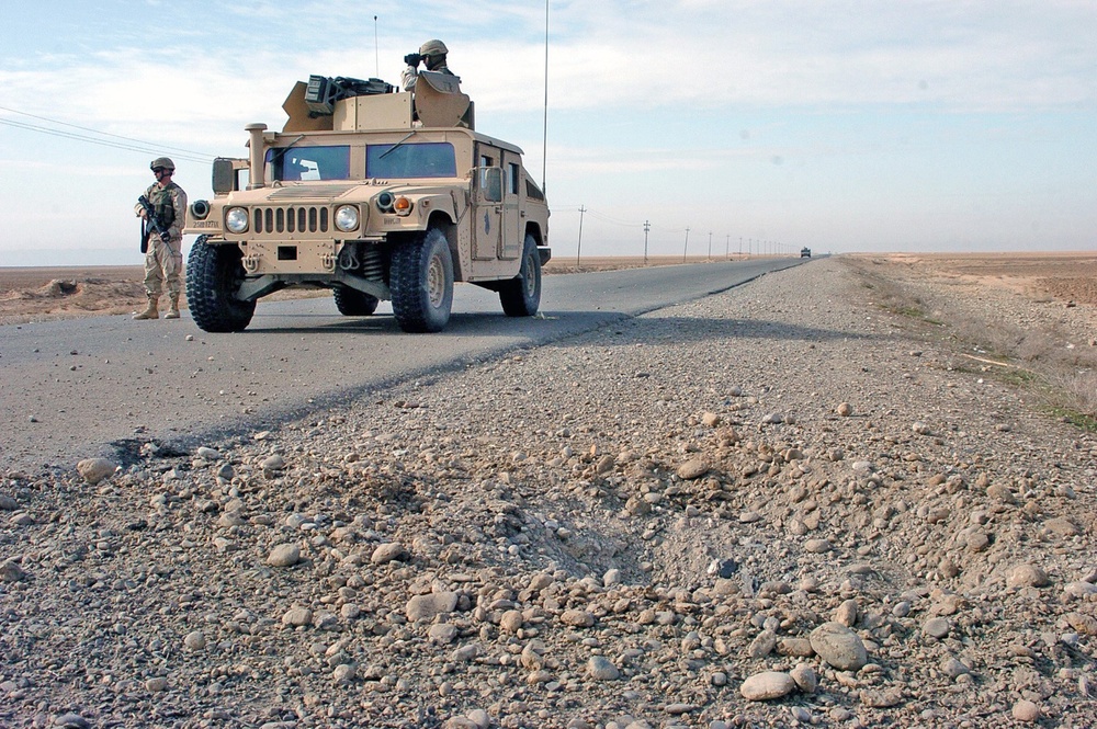 An IED crater lies on the shoulder of a road