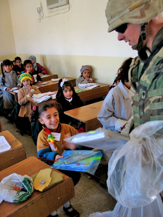 A Soldier hands a packet of school supplies