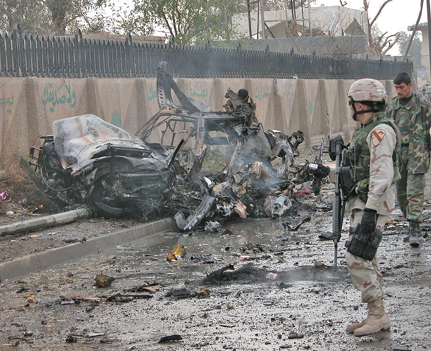 A Soldier looks at the remains of a car