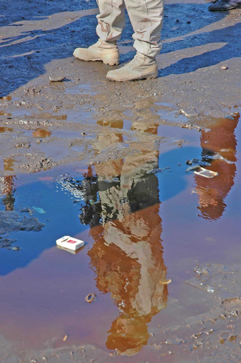 The reflection of a Soldier ripples in a puddle of kerosene