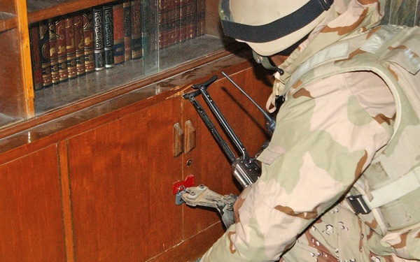 An Iraqi National Guardsman cuts the lock to a cabinet