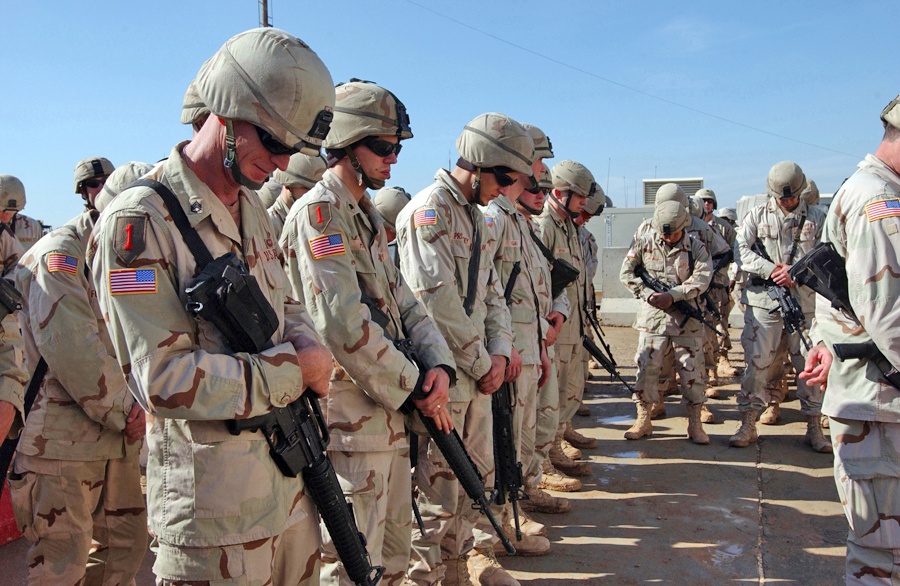 Soldiers bow their heads in respect during the opening prayer