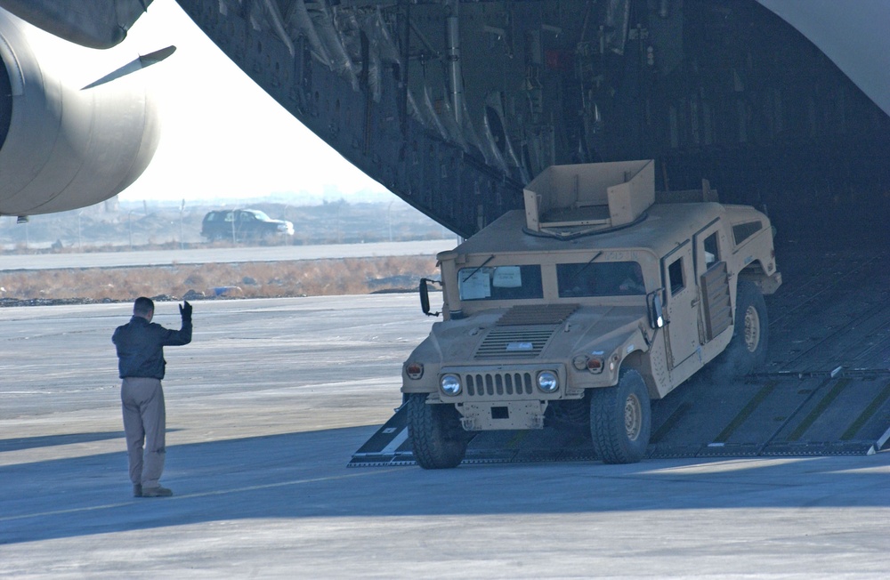 An Airman ground guides a HMMWV off  a C-17