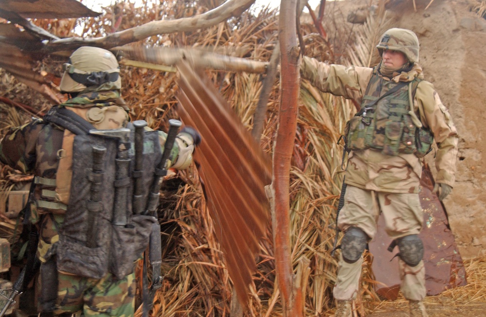 Soldiers search the yard of a known criminal in a village