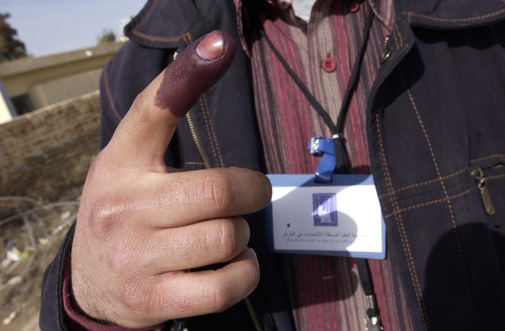 An Iraqi polling center worker holds up his index finger