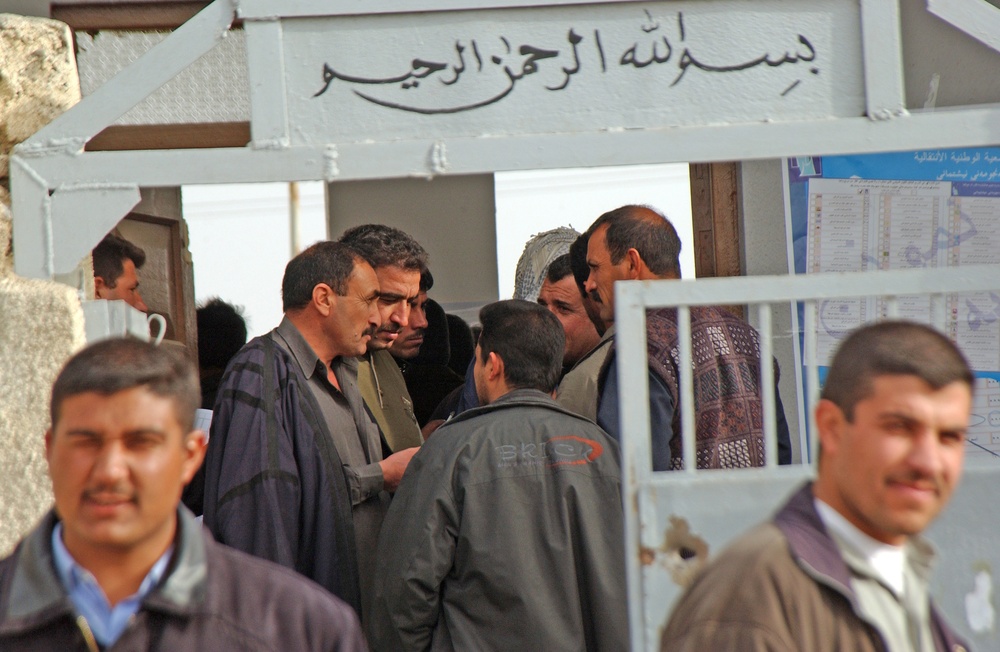 Iraqi voters talk while they wait inside of a polling station