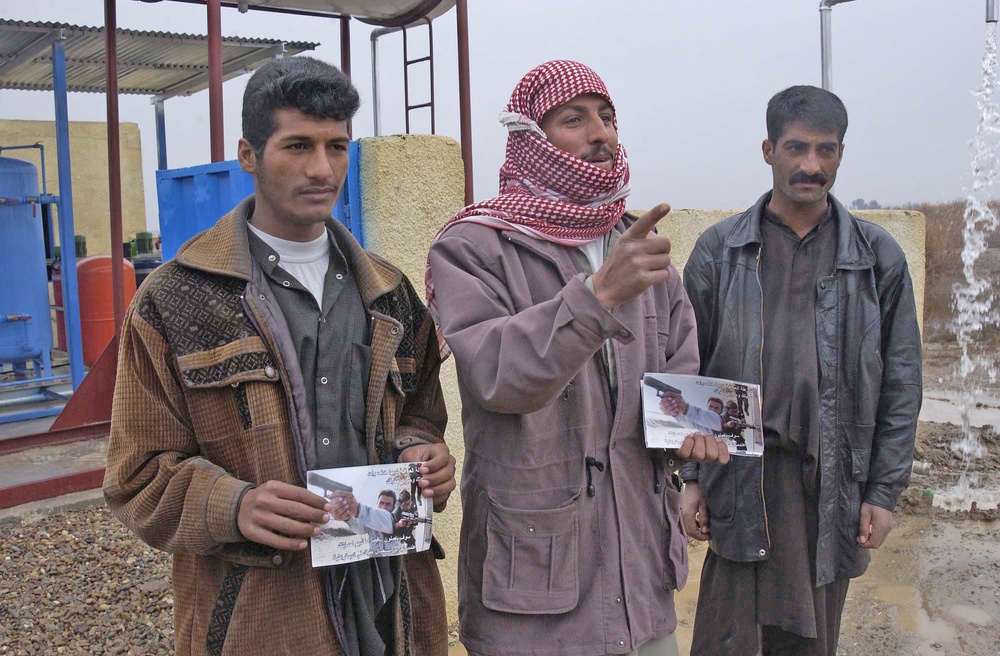 Three Iraqi men stand in front of a water pump