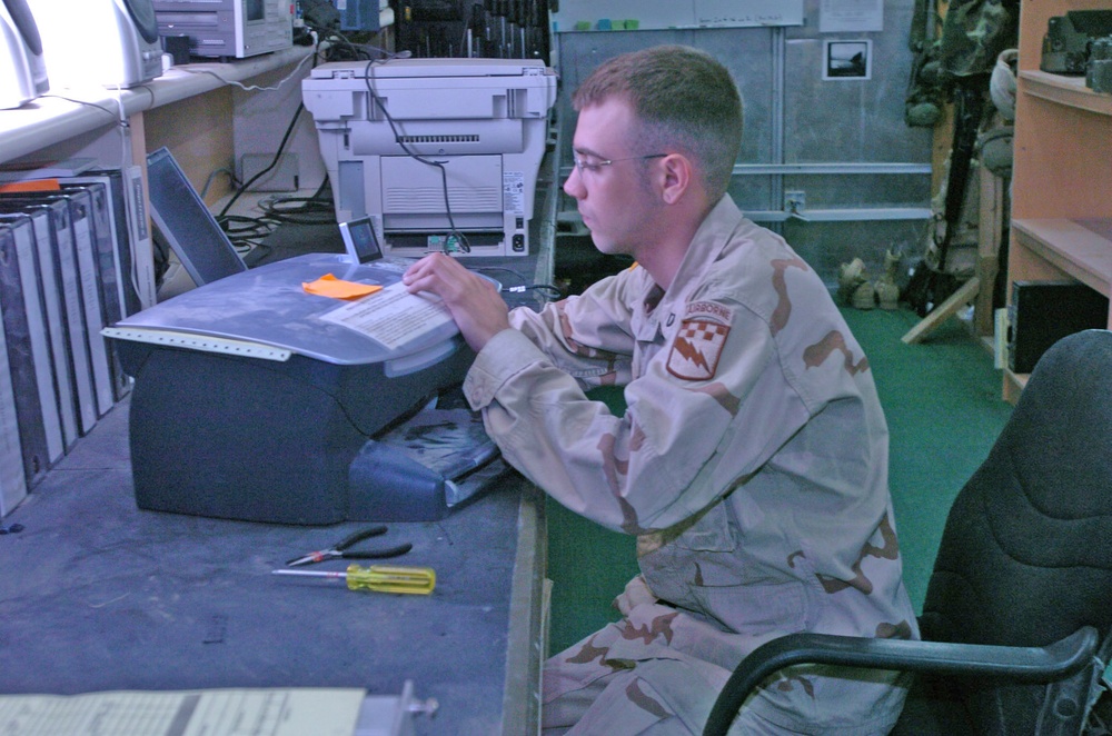 Pfc. Logan M. Radish works on a broken printer