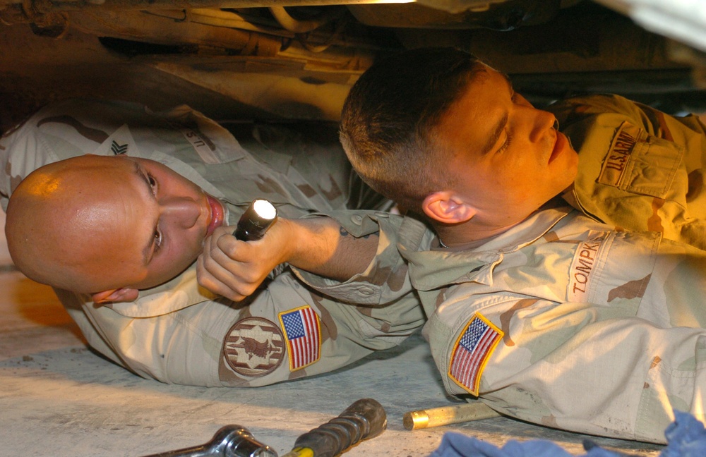 Two soldiers begin replacing the gearbox of an armored humvee