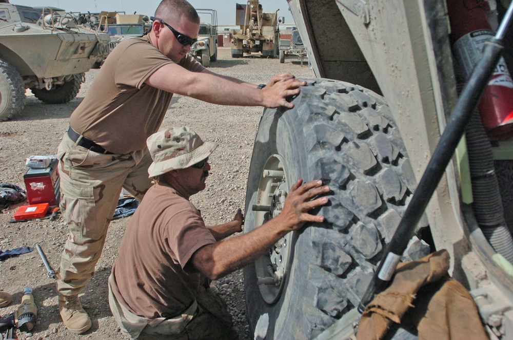 Two soldiers put a tire back on the 940th M1117