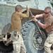 Two soldiers tighten down the lug nuts on their M1117