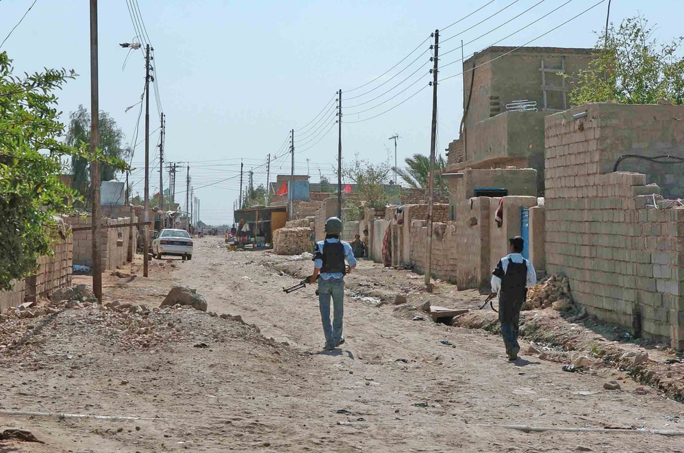 Iraqi Police officers secure an alley during a raid in Awhida