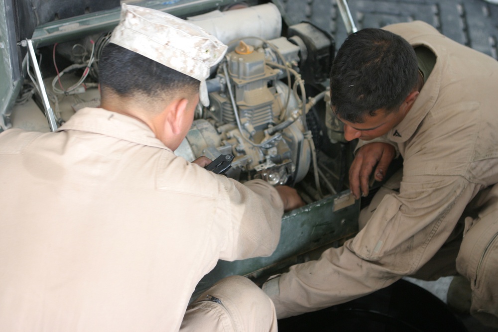 Two soldiers change the oil in one of the many generators