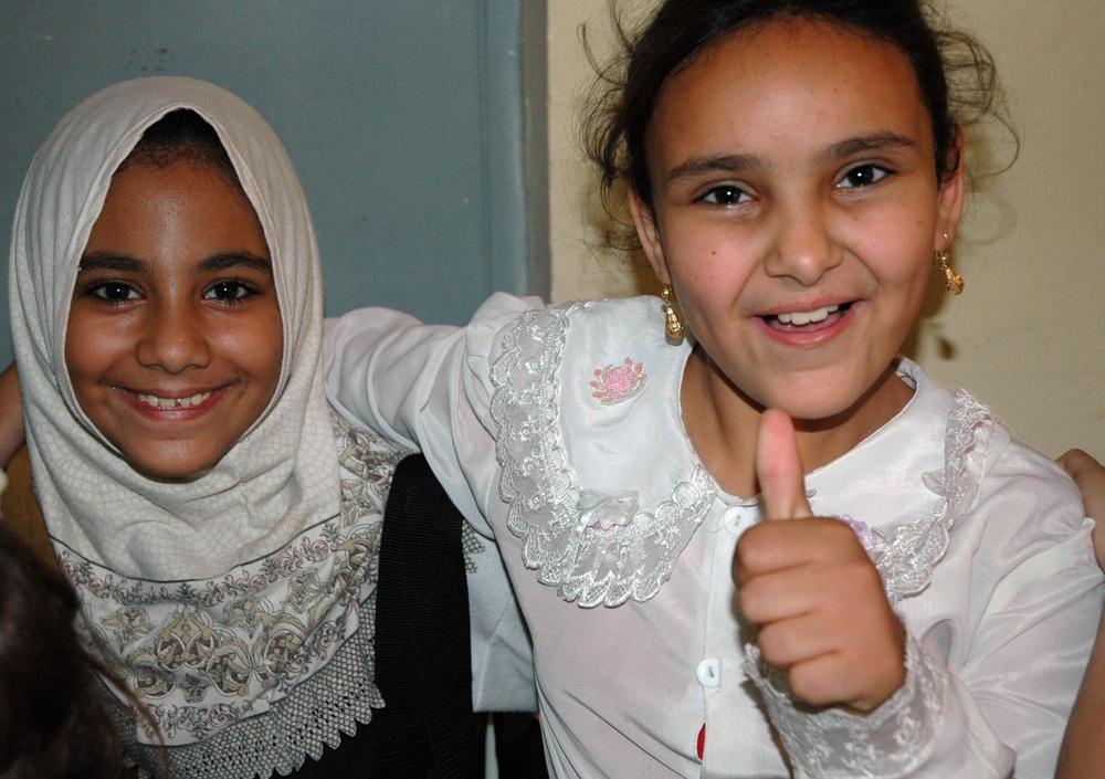 An Iraqi school girl gives the thumbs up alongside her friend