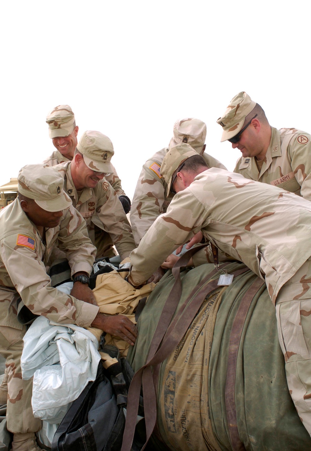 Soldiers try to stuff a large drash tent into its cargo bag