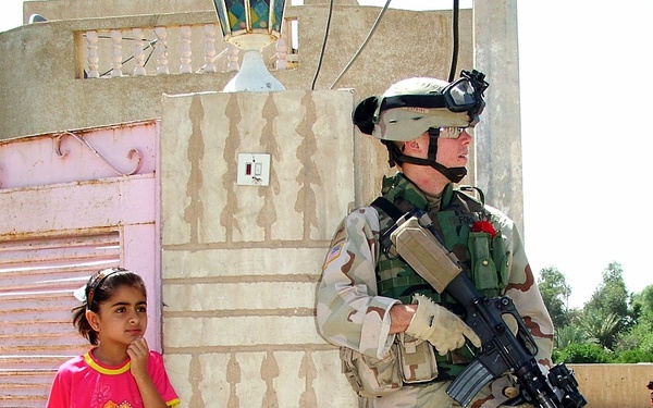 Sgt. Ford watches a neighborhood street with an Iraqi girl