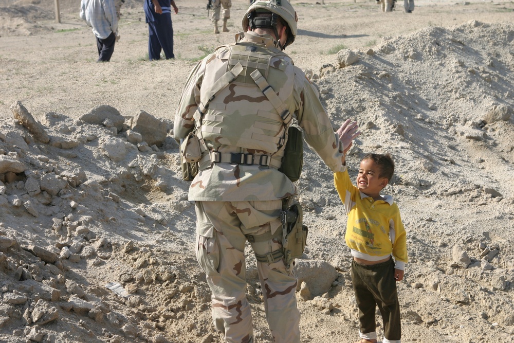 A soldier (high-fives) a local Iraqi boy