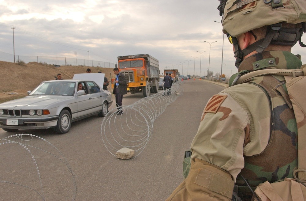 A Soldier watches as a Iraqi police search a vehicle