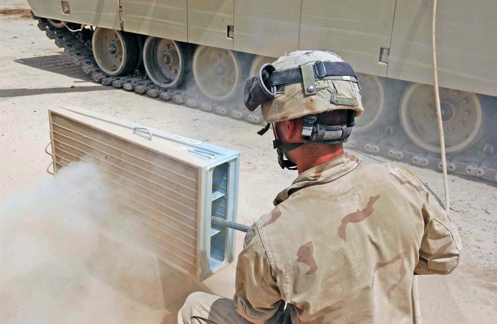 A soldier uses an air wand to remove the dirt from the tank's V-