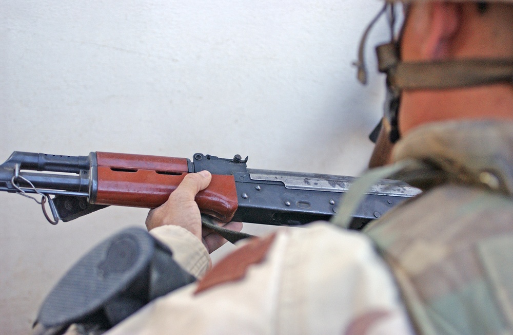 A soldier examines an AK 47 found during a raid