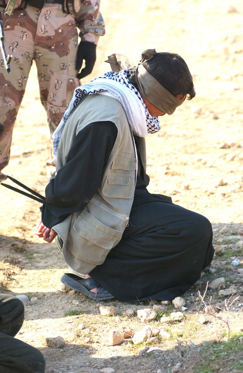 A detained Iraqi man kneels just off the roadway