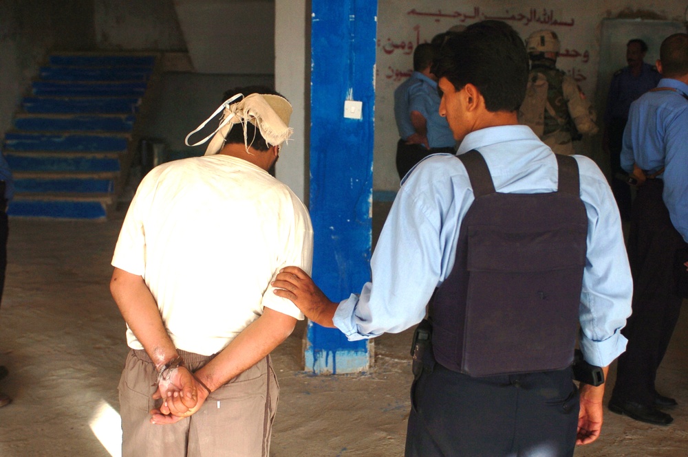 an Iraqi Policeman escorts a detainee at a Tikrit Police Station