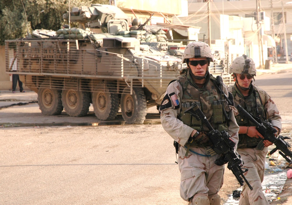 SSG Emery and PFC Little walk in front of their Stryker during a