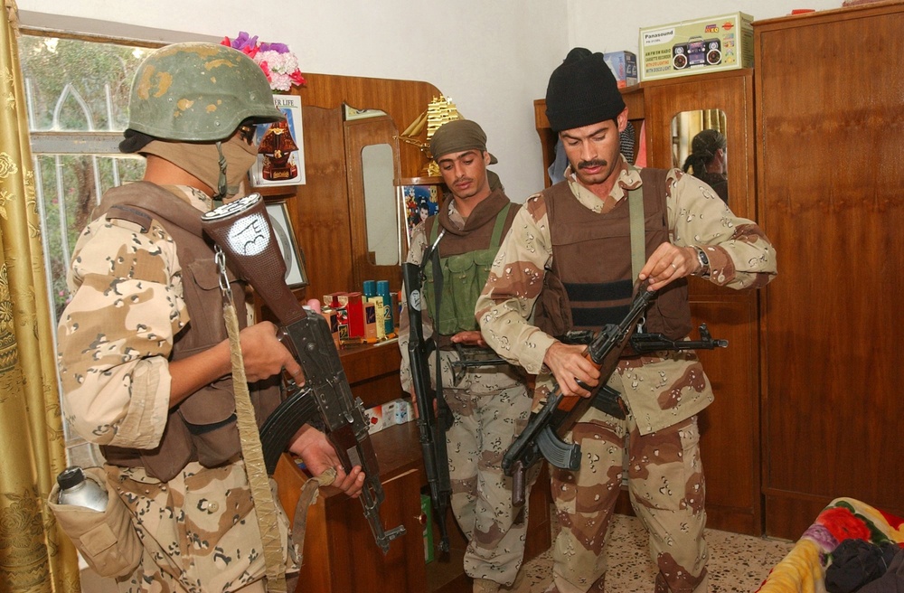 IA Soldiers inspect an assault rifle found in a the closet of a home