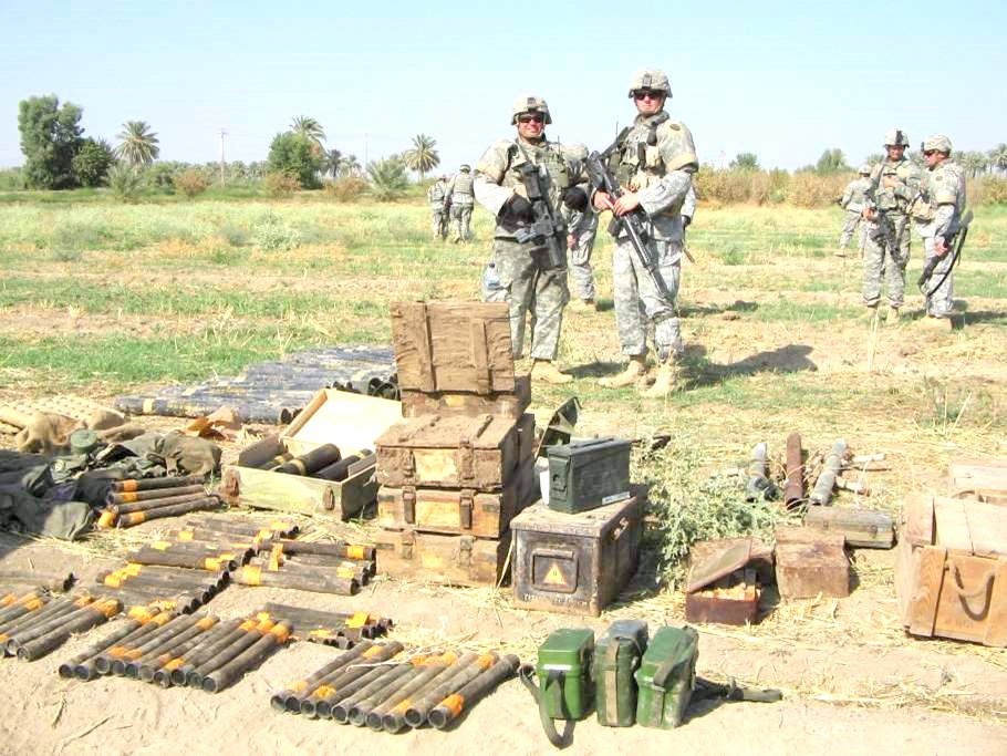 Soldiers stand before a discovered weapon cache