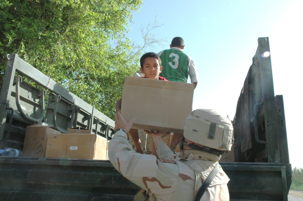 Children rush to help Soldiers unload boxes packed with school supplies