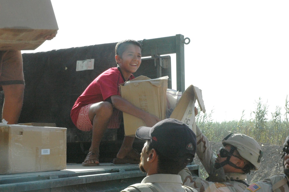 Children rush to help Soldiers unload boxes packed with school supplies