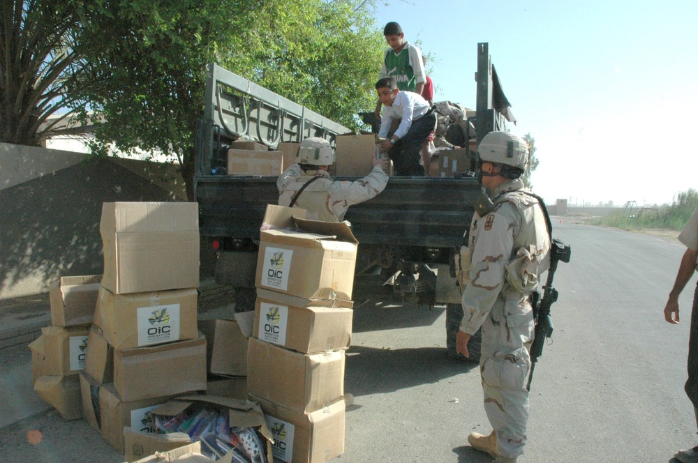 Children rush to help Soldiers unload boxes packed with school supplies